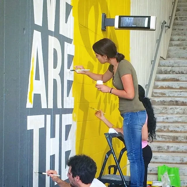Artists painting a large mural on a building exterior.